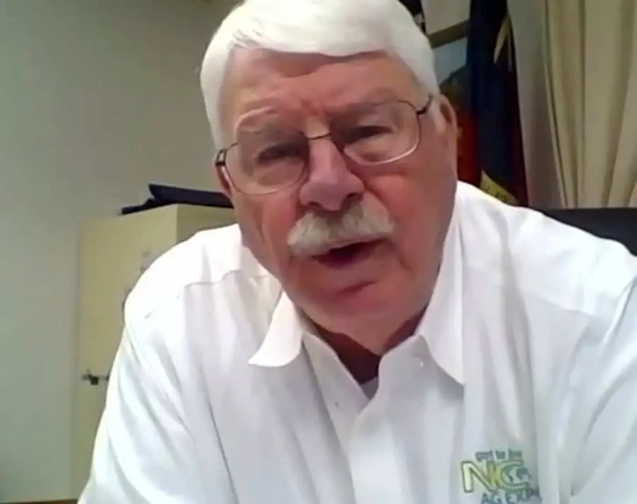A senior man with white hair and glasses speaking in an office setting.