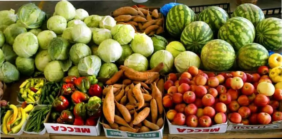Fresh green and yellow zucchinis, watermelons, sweet potatoes, and apples displayed at a market stal.