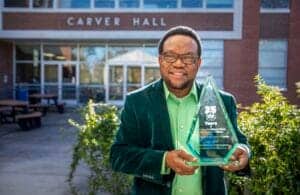 CAES News award recipient holding a glass trophy outside Carver Hall.