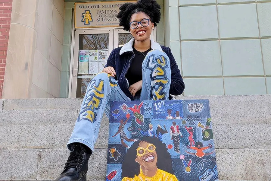 Diverse student sitting on school steps with a colorful CAES News tote bag.