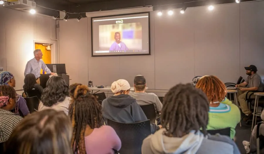 A teacher giving a presentation to a diverse group of students in a classroom setting.