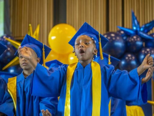 Graduation children in blue caps and gowns celebrating achievement at school ceremony.