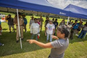 Community outdoor event with diverse group under blue canopy in grassy field.