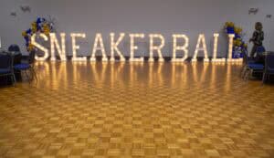 Bright marquee letters spelling "SNEAKERBALL" in a decorated event space with wooden flooring and seating.