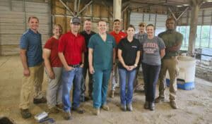 A group of eleven people in a barn, wearing various work attire, smiling and posing for the photo.