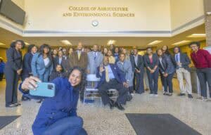 A diverse group of students and faculty poses for a selfie in a university building's lobby.