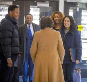 Five people engaging in a lively conversation indoors, smiling and dressed warmly.