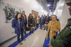 A diverse group of people listens and talks in a hallway, with a historical photo displayed on the wall.