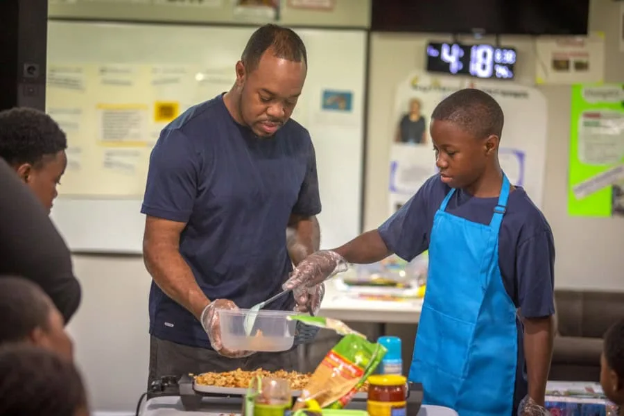 Man and boy cooking together in a community kitchen or cooking class setting.