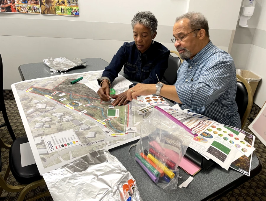 Karen and Kevin Truitt collaborate on a site plan for Benbow Park, seated at a table with a large map spread out in front of them. They are using markers and design elements to create their vision of the park.