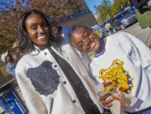 Two smiling women wearing CAES branded apparel outdoors on a sunny day.