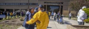 A woman and a man wearing yellow jackets talking outside D.C. Webb Hall during a busy campus event.