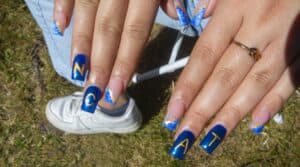 Nail art featuring deep blue and gold designs with letters "N," "C," "A," and "T" on long acrylic nails.