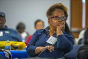 Thoughtful woman attending a conference, listening attentively with a hand on her face, surrounded b.