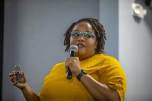Accessible microphone presentation at a conference, woman in yellow dress speaking to audience, enga.
