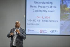 A speaker discusses heirs' property at the 2024 NC A&T Small Farmers Conference with presentation slides in the…