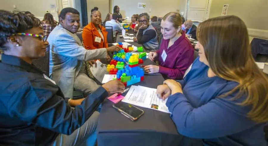 Attendees at the 2024 Grassroots Leadership Conference participate in a hands-on activity with colorful Lego blocks during a workshop session. Seated at a table, they engage in discussion and collaboration, surrounded by conference materials.
