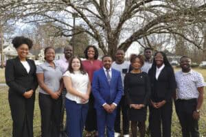 A diverse group of eleven individuals poses outdoors, smiling in front of a bare tree.