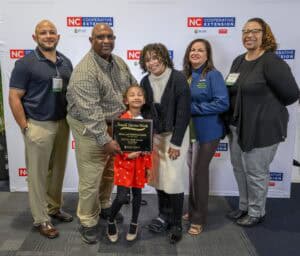A family and friends proudly celebrate receiving the Small Farmers of the Year award, holding a plaque together.