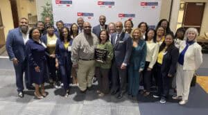 Large group of people standing together in front of an NC Cooperative Extension step-and-repeat banner, with two individuals in the center holding a Small Farms Week plaque; all are smiling and dressed in business or professional attire.