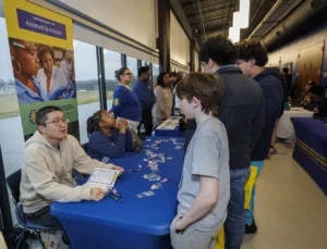 Students engage with representatives at a university event, learning about the Department of Animal Sciences. Tables are filled with informational materials and items to take. People interact in a well-lit indoor space.