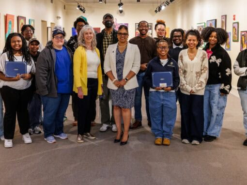 A diverse group of people at an art gallery, holding notebooks and smiling for the photo.
