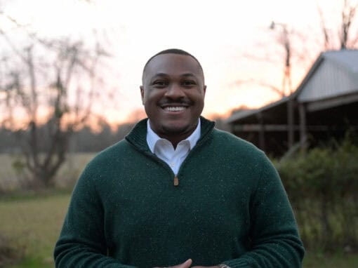 Smiling man outdoors during sunset in a green sweater and white shirt.