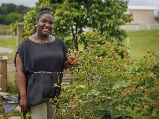 Woman smiling in a garden with green plants and trees in the background.