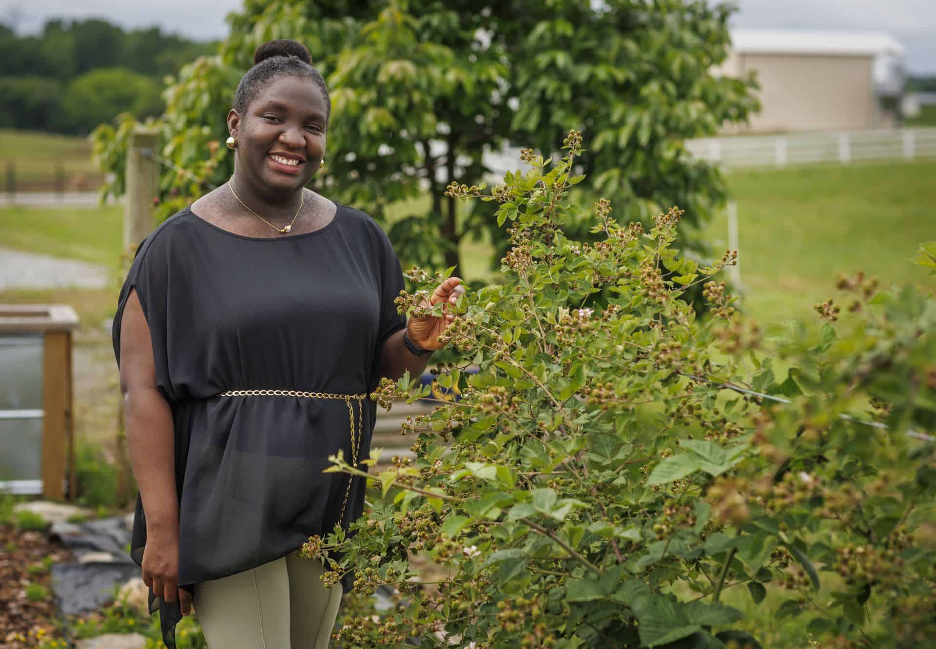 Woman smiling in a garden with green plants and trees in the background.