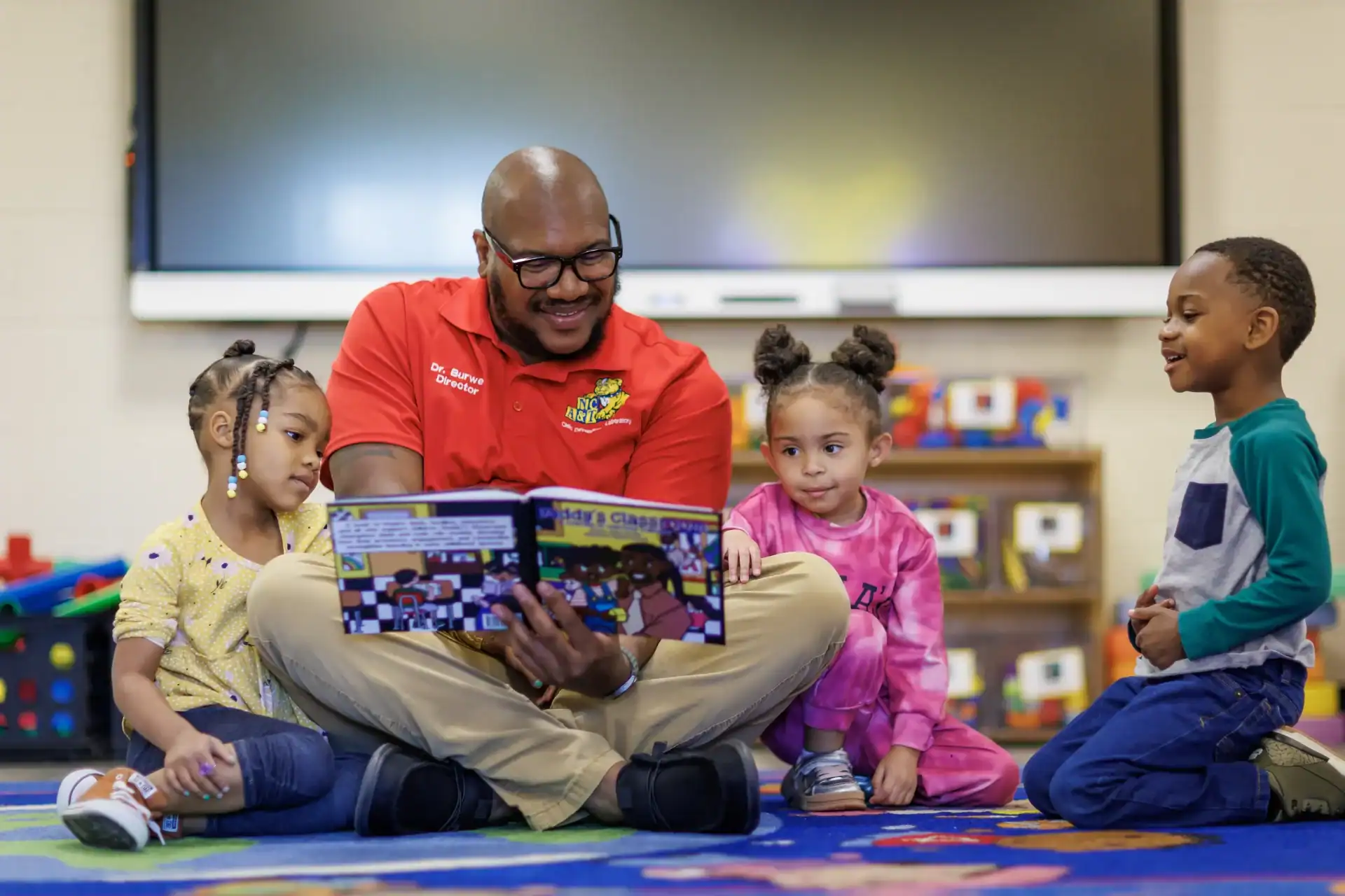 Teacher reading a book to young children in a classroom setting.