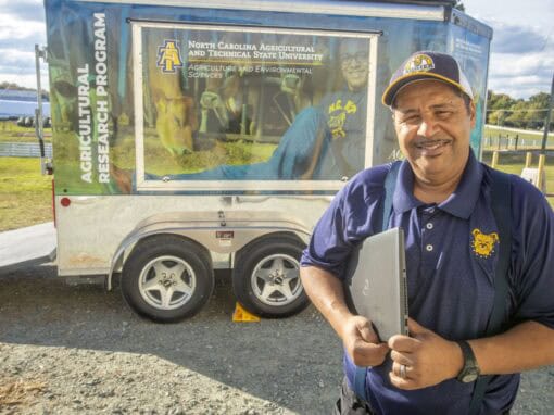 Man in blue uniform smiling in front of North Carolina Agricultural and Technical State University.
