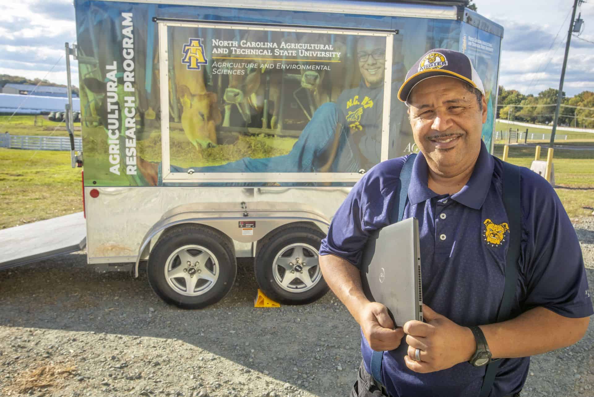 Man in blue uniform smiling in front of North Carolina Agricultural and Technical State University.