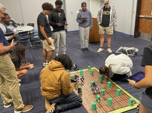 Group of young people playing a game with cups and tokens on a wooden board in a room.
