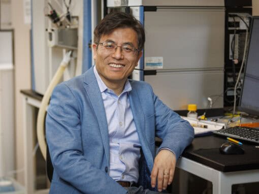 Scientist smiling in a laboratory with scientific equipment and computers.