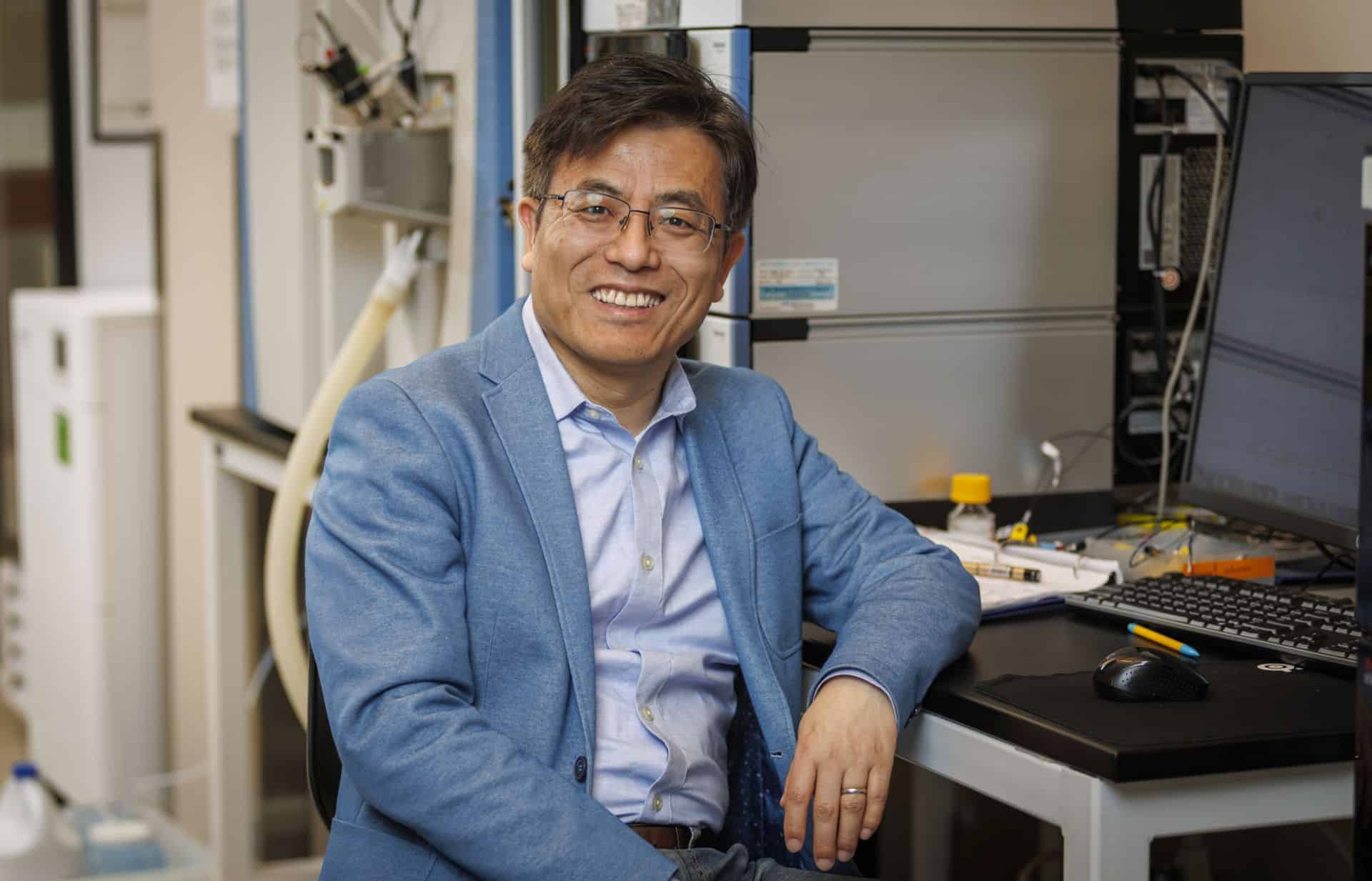 Scientist smiling in a laboratory with scientific equipment and computers.