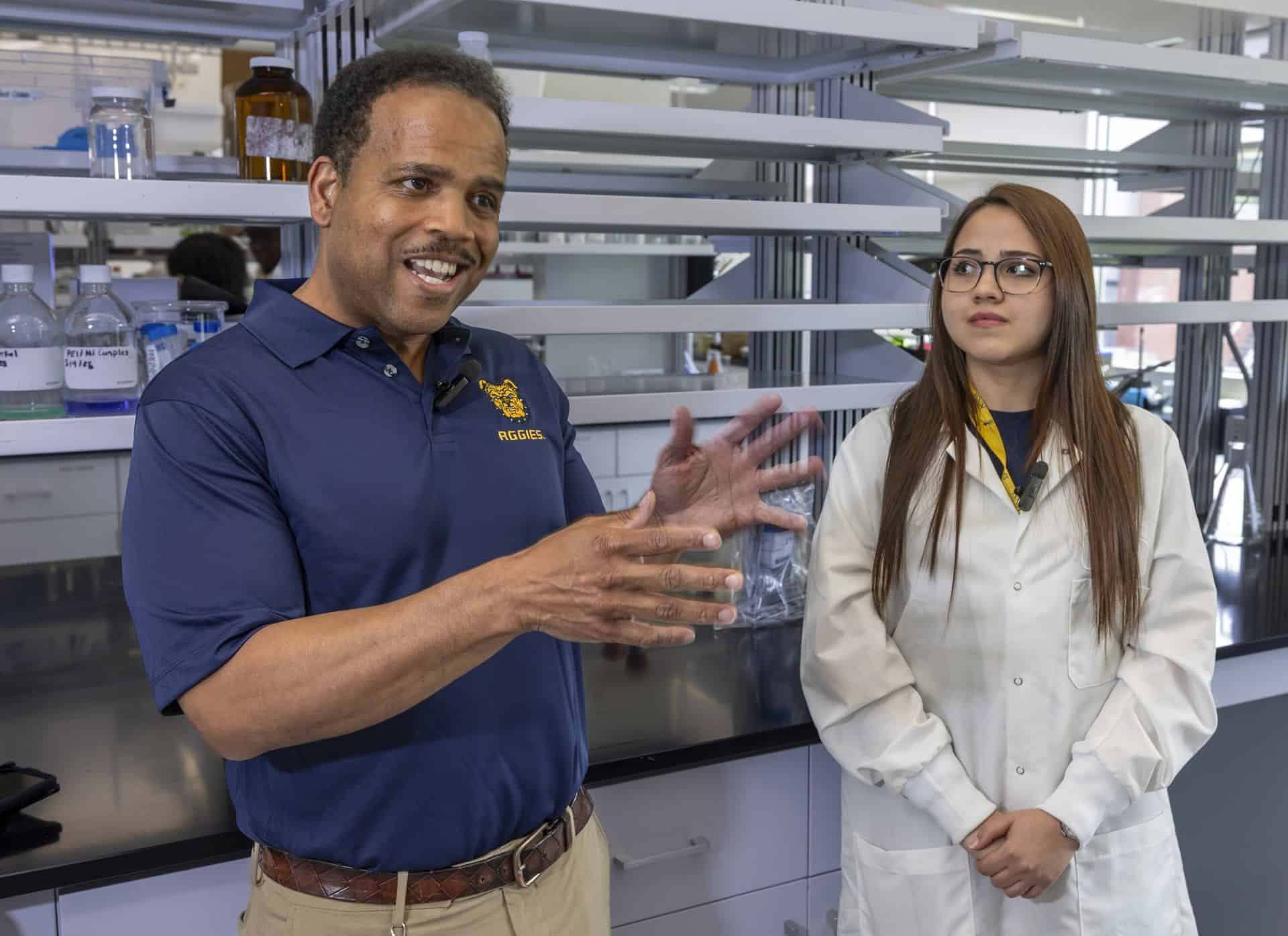 Scientists discussing in a laboratory with scientific equipment and shelves.