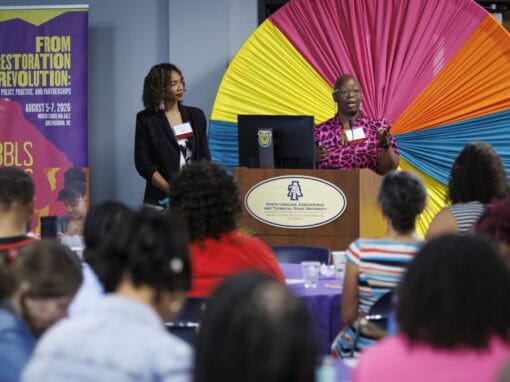 Diverse speakers at a conference with colorful backdrop and audience.