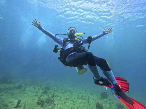 Scuba diver underwater with arms outstretched, exploring ocean floor.
