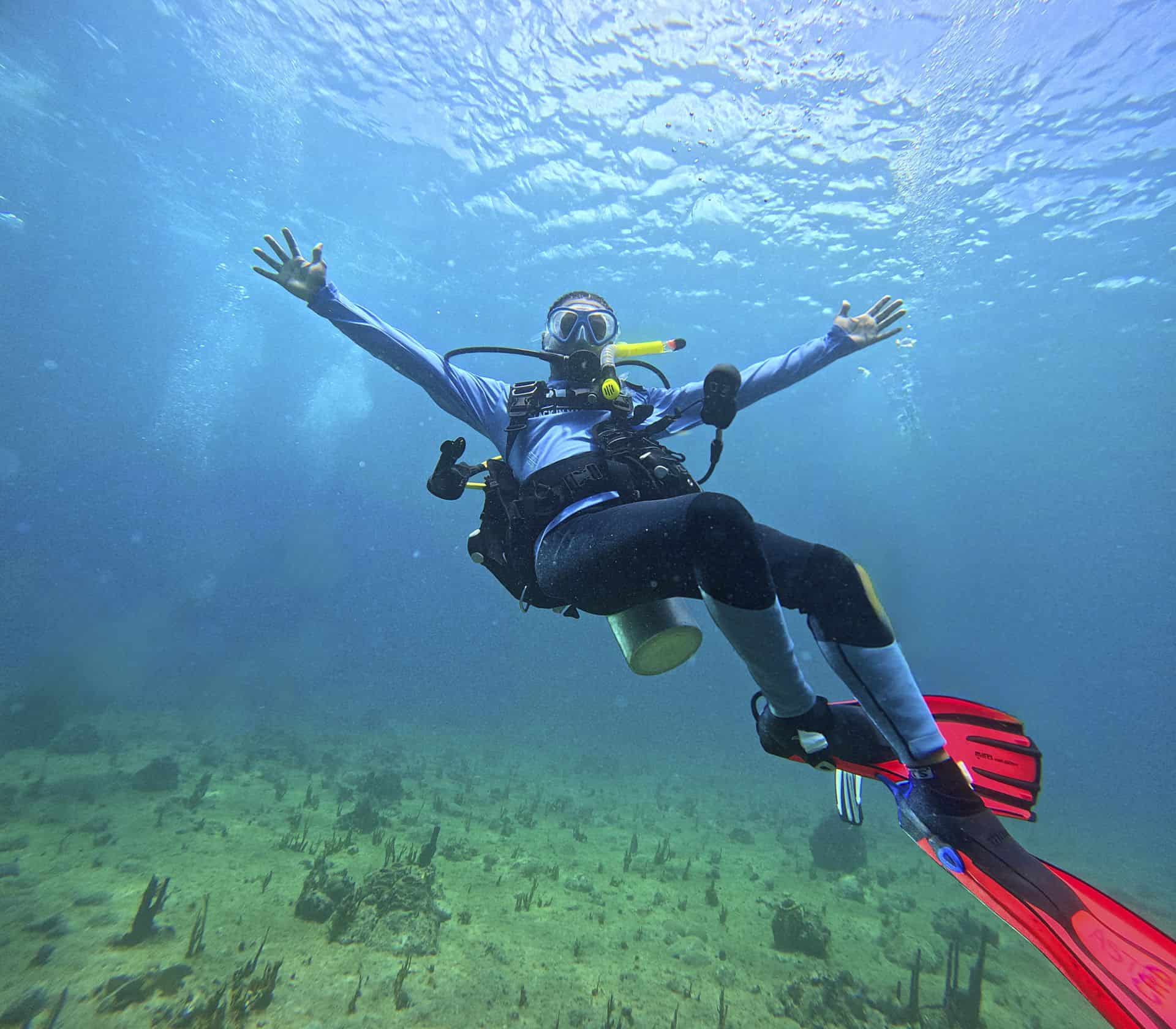 Scuba diver underwater with arms outstretched, exploring ocean floor.