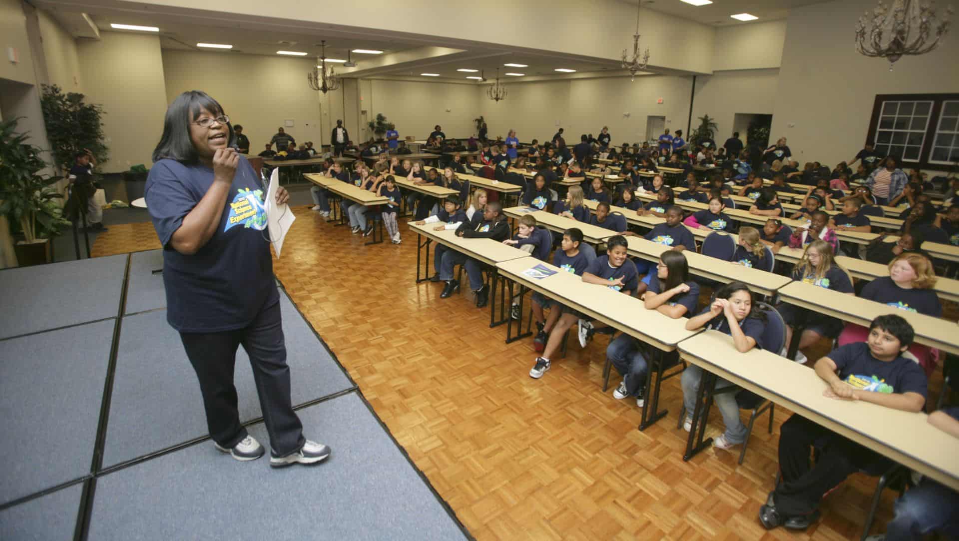Speaker addressing a large group of students in a spacious hall.