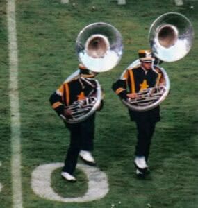 Marching band members playing sousaphones on a football field.