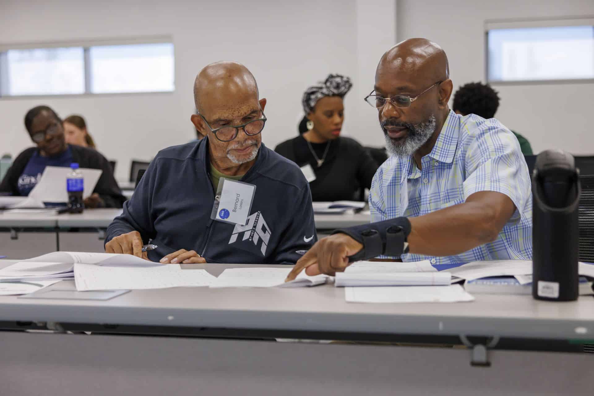 10_01_2026_360 Leadership 010 – resized Two men collaborate over documents at a workshop or conference table.