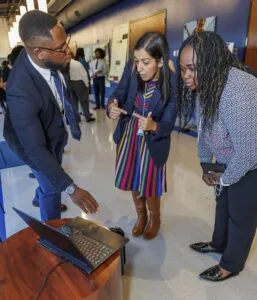 Three individuals engaged in a discussion near a laptop during a presentation event.